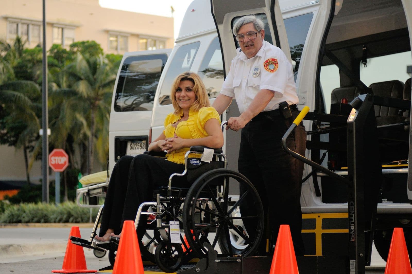 A uniformed attendant assisting a seated passenger onto the lift of an accessible van
