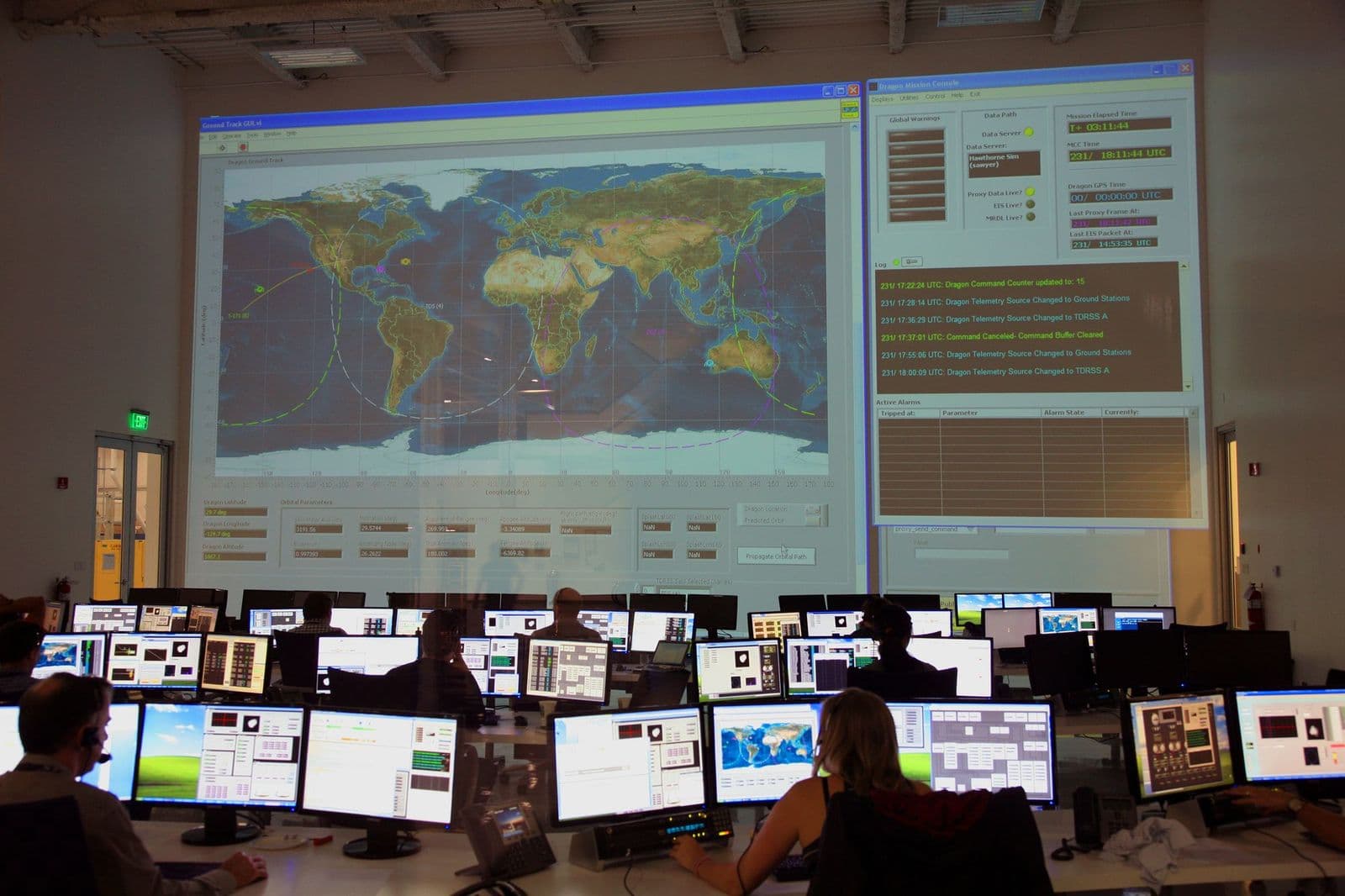 A dispatch room with rows of operators at monitors in front of a large map display