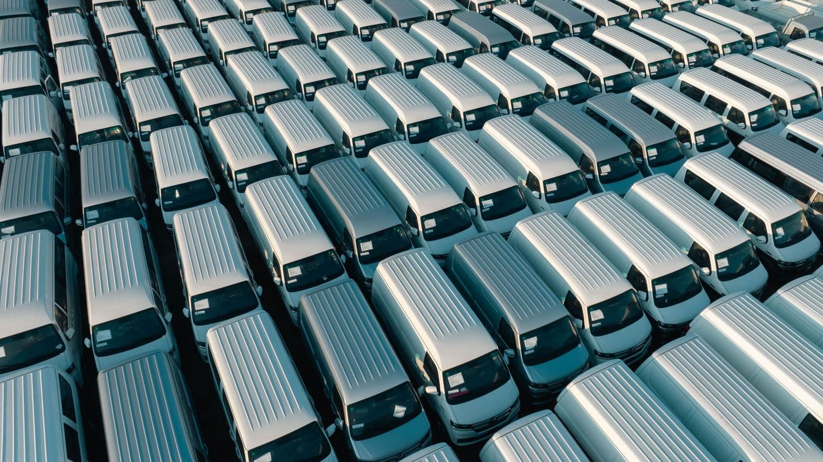 Rows of identical white vans parked in a depot lot, seen from above