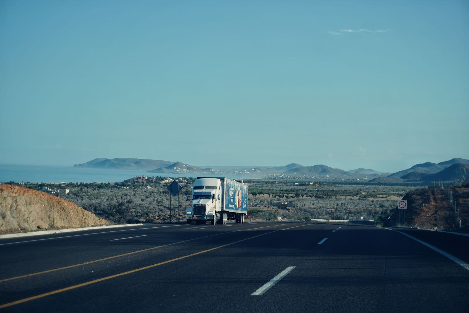 A semi-truck on an open highway with mountains on the horizon