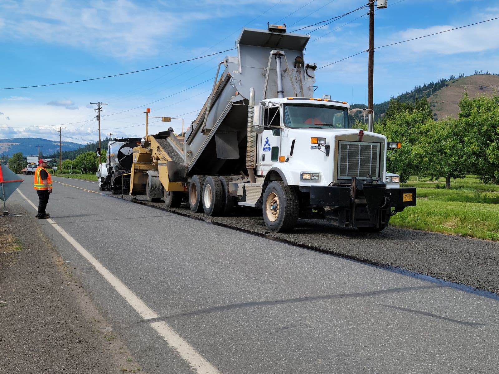 A public works crew and paving equipment working on a road
