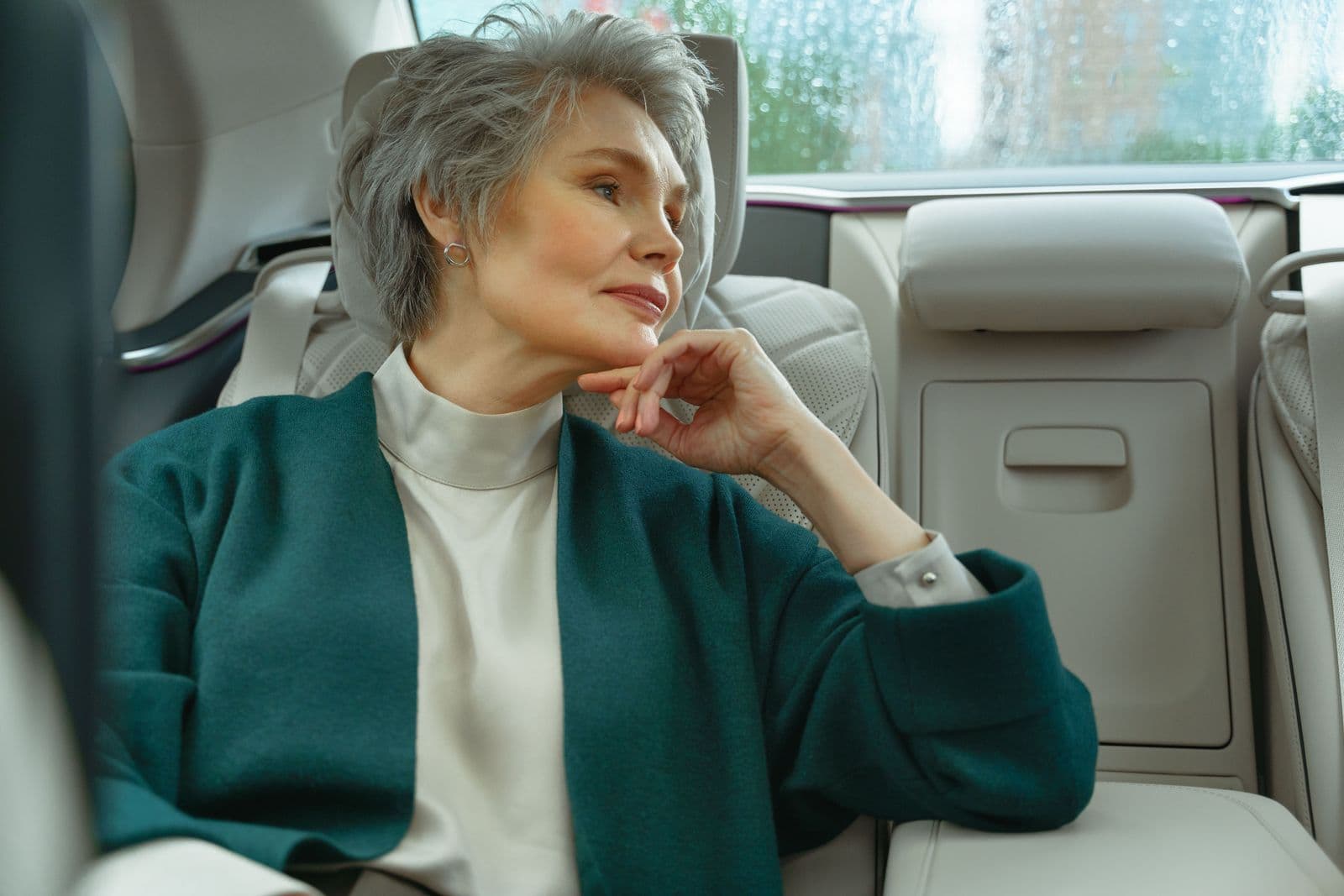 An older woman seated comfortably in the back of a car, looking out of the window
