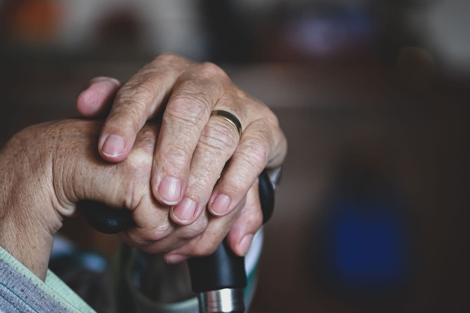 An older person's hands resting clasped on the handle of a walking cane