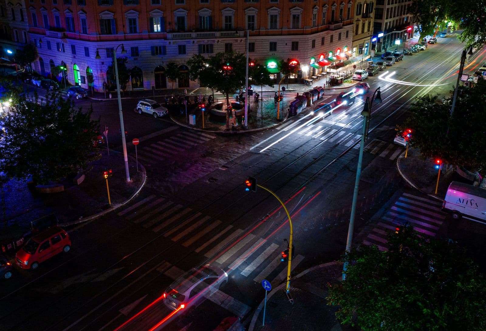 A city intersection at night seen from above, with light trails from moving traffic