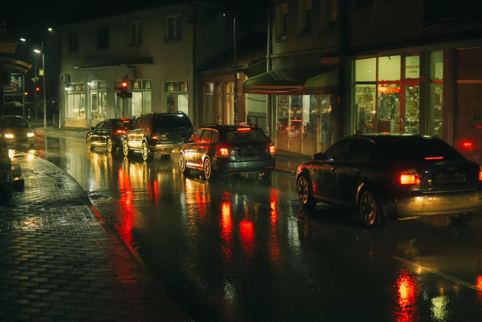 Cars queued on a wet city street at night with brake lights reflecting on the road
