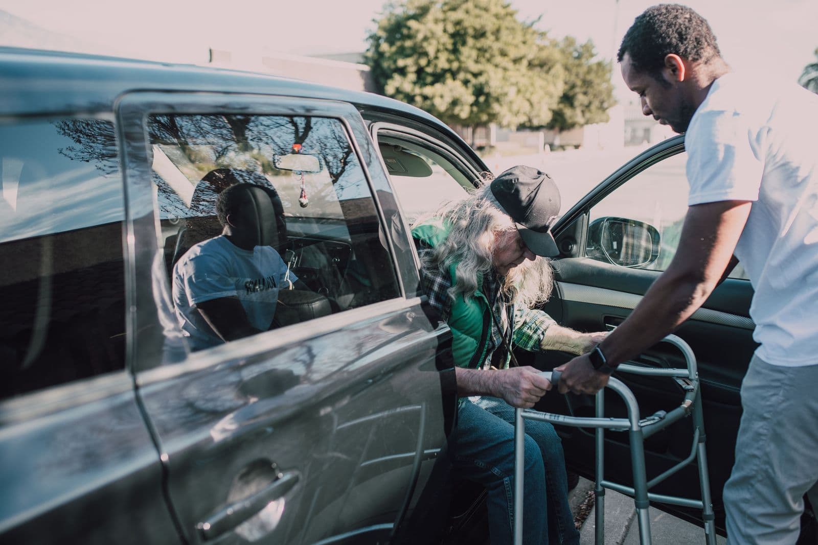 A care worker steadying a walker as an older man gets out of a vehicle at the curb