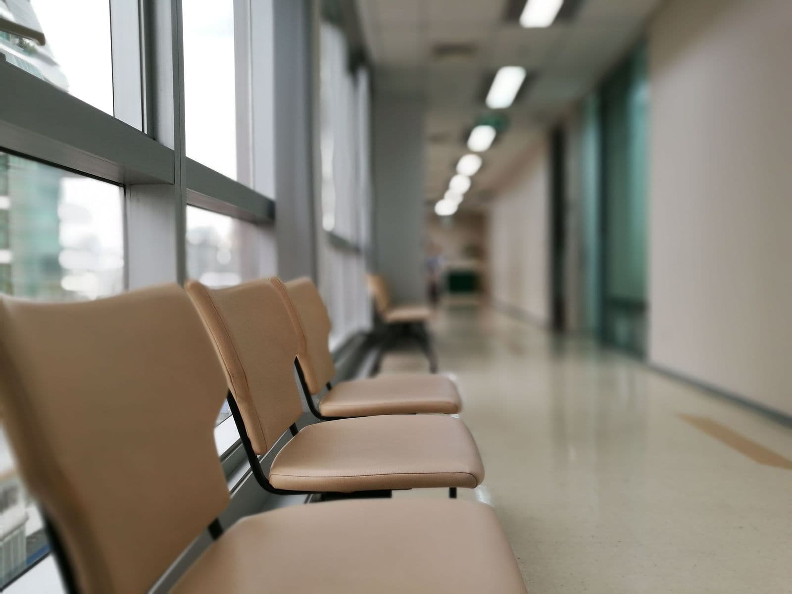 An empty row of chairs in a hospital waiting area beside a window