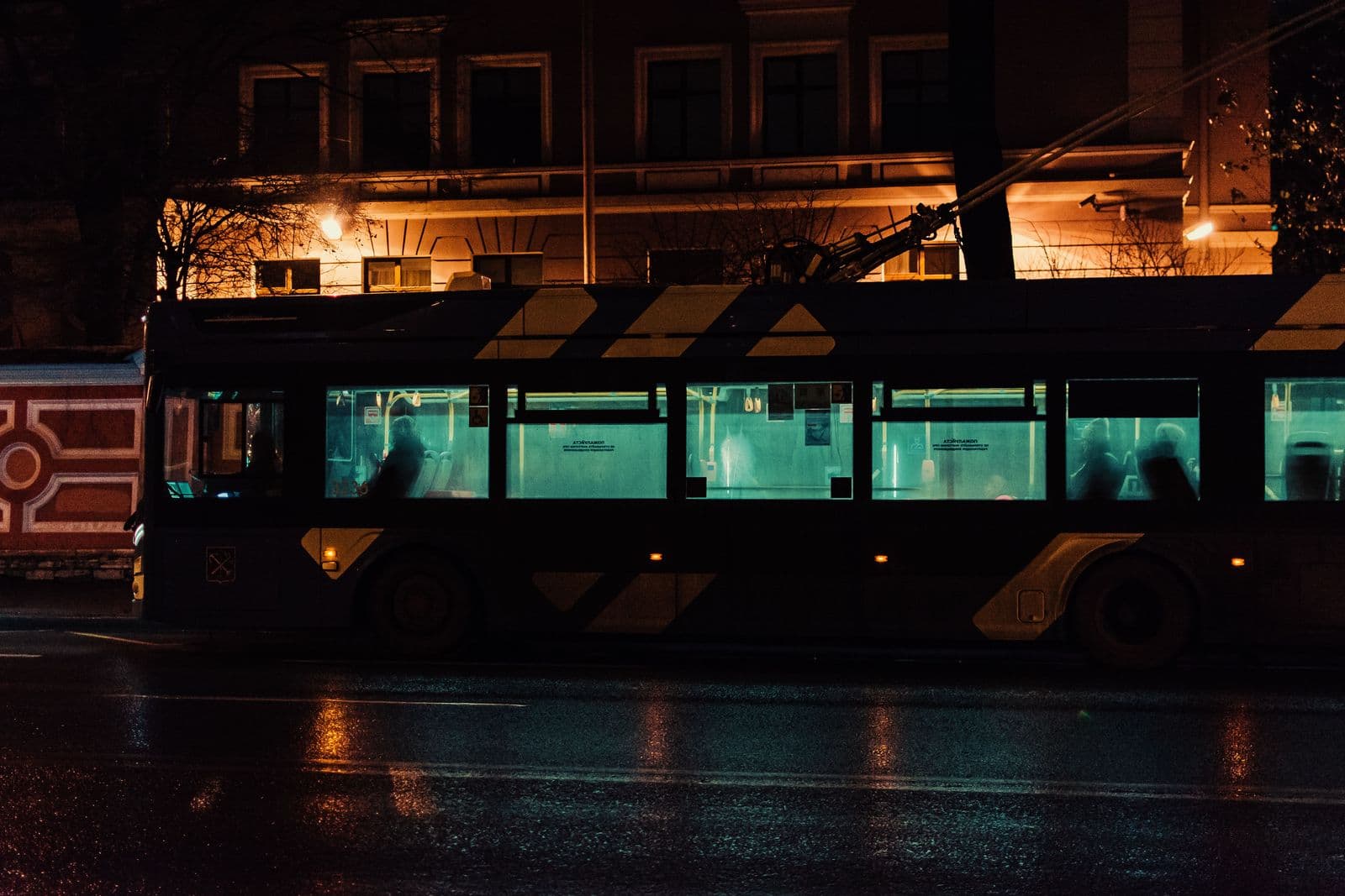 A lit city bus moving along a wet street late at night